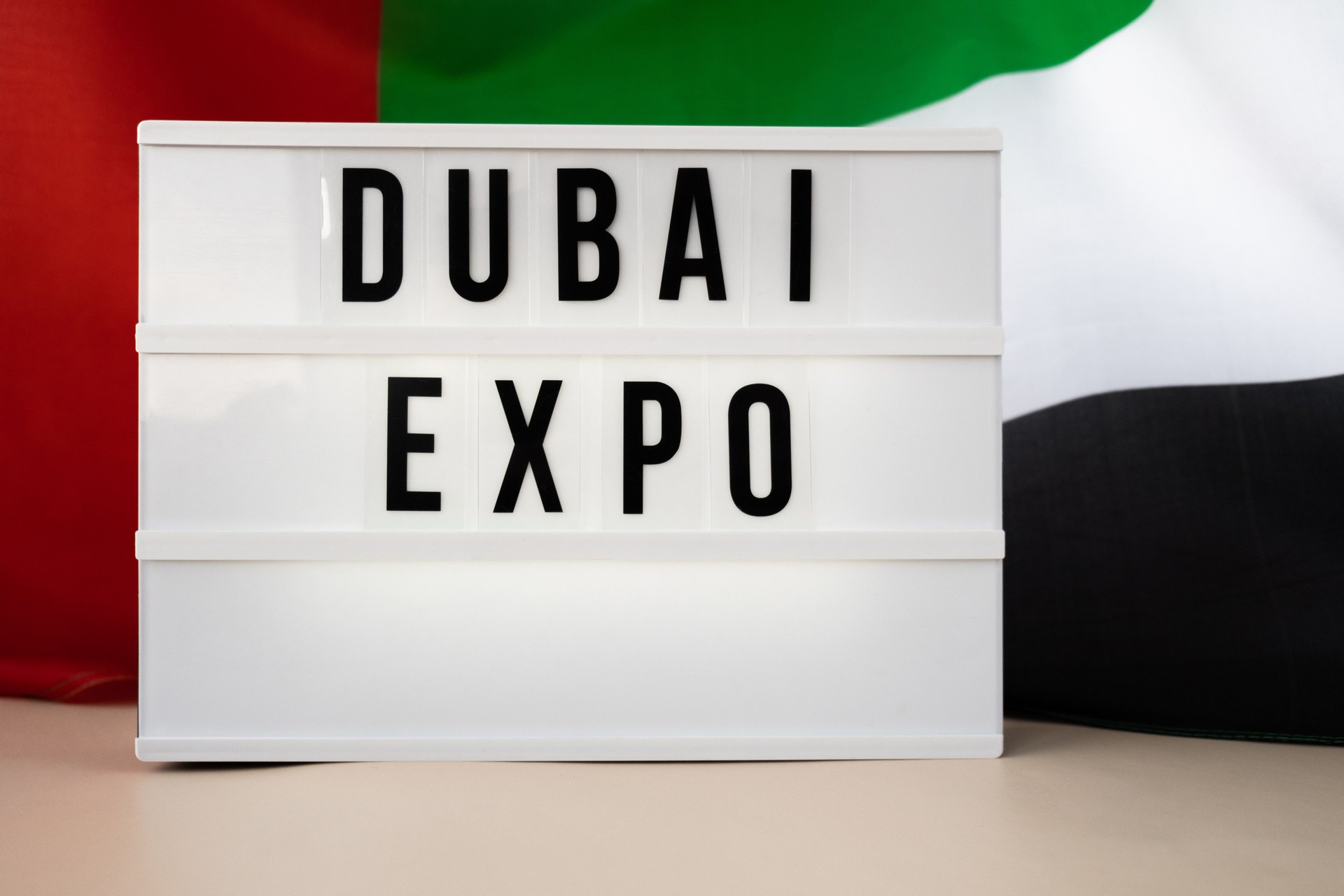 Message text DUBAI EXPO on background of waving UAE flag made from silk. United Arab Emirates flag with concept of tourism and traveling. Inviting greeting card, advertisement